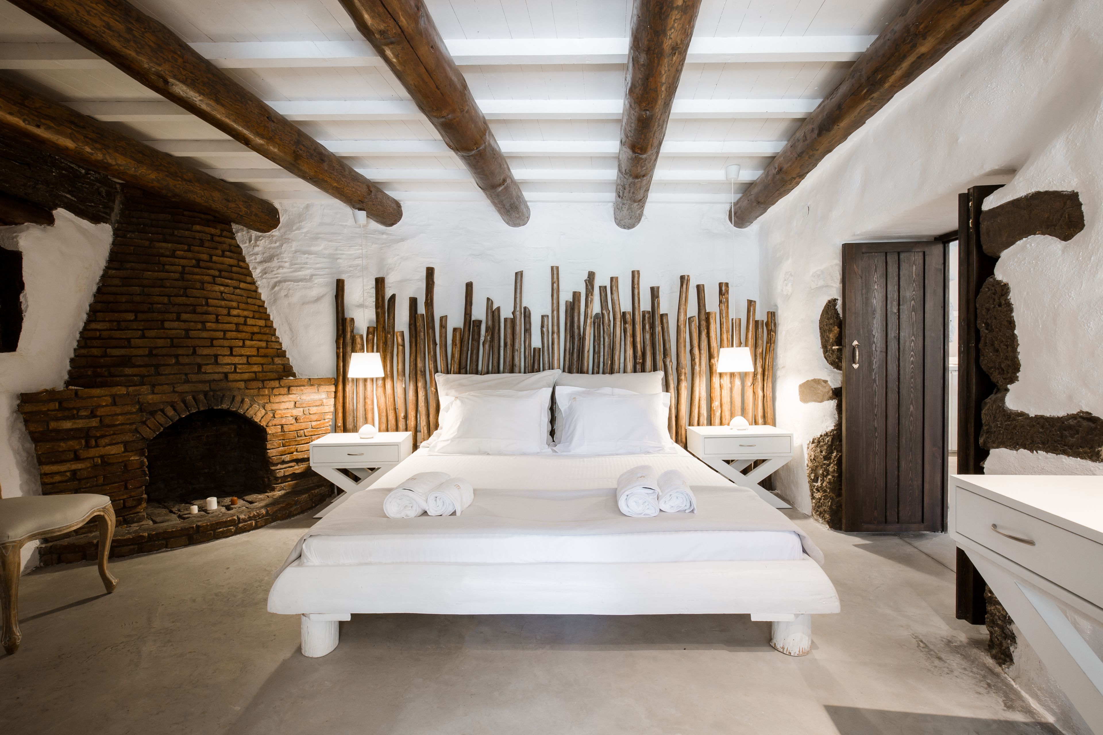 Een slaapkamer met een groot bed, een schouw van baksteen, houten balken en een rustieke deur.