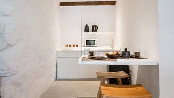 Una cocina compacta con paredes blancas, vigas de madera a la vista, una encimera blanca y un taburete de madera.