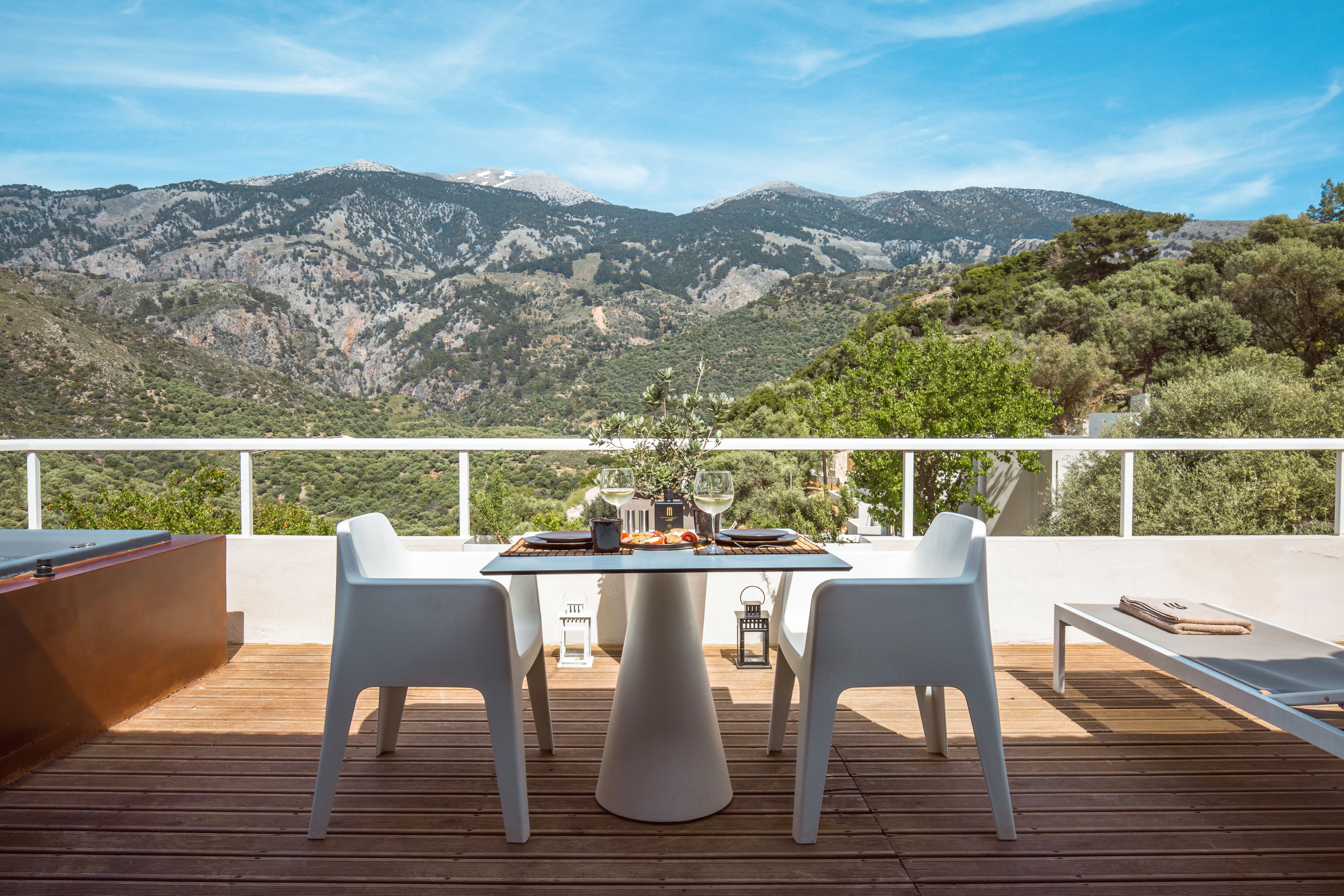 A terrace with a table set for dining, overlooking a mountainous landscape.