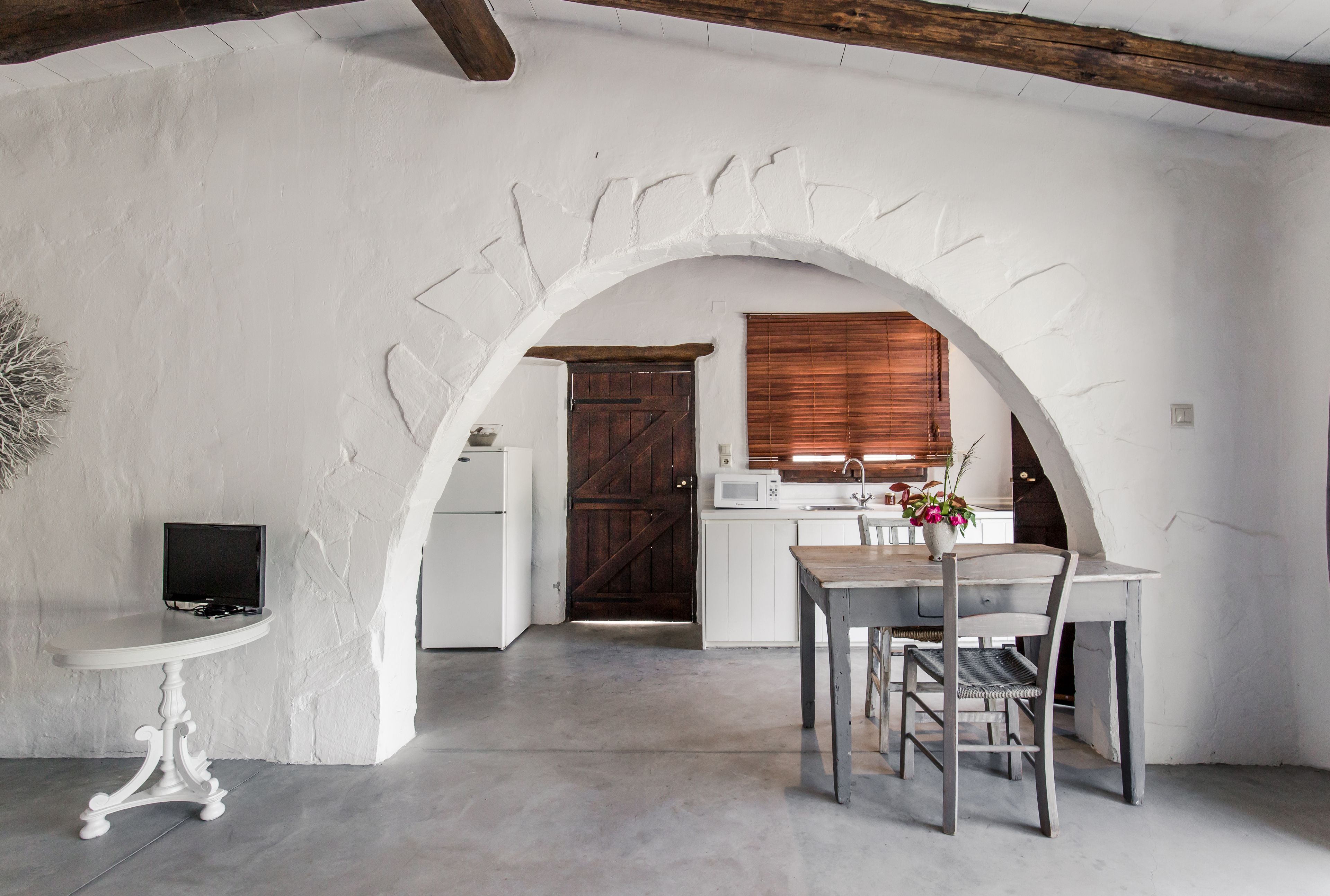 Uma cozinha rústica com paredes brancas, uma porta de madeira e um espaço de refeições com mesa e cadeiras.