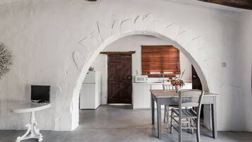 Uma cozinha rústica com paredes brancas, uma porta de madeira e um espaço de refeições com mesa e cadeiras.