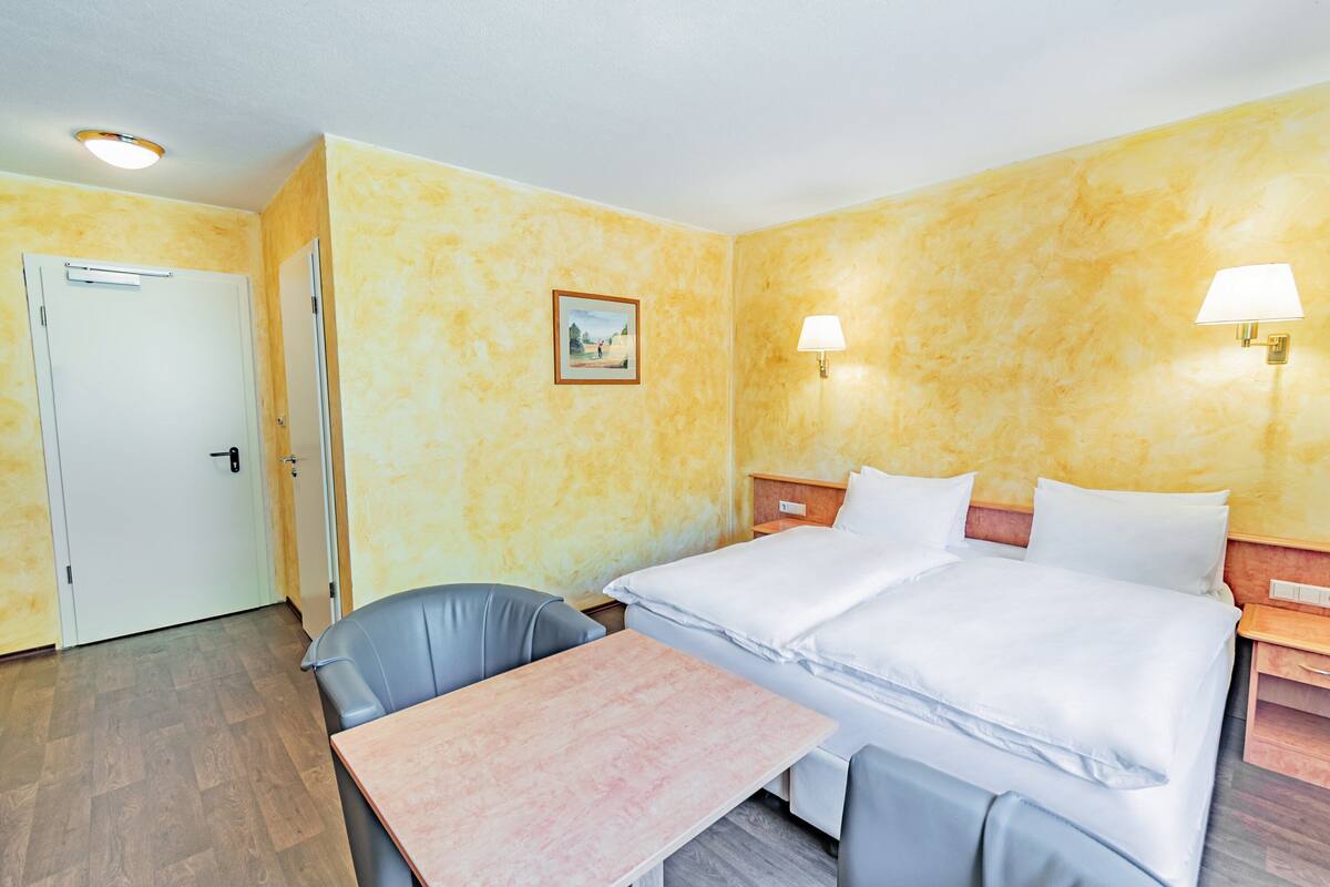 Ein Hotelzimmer mit Bett, Tisch, Stuhl und einem Bild an der Wand.