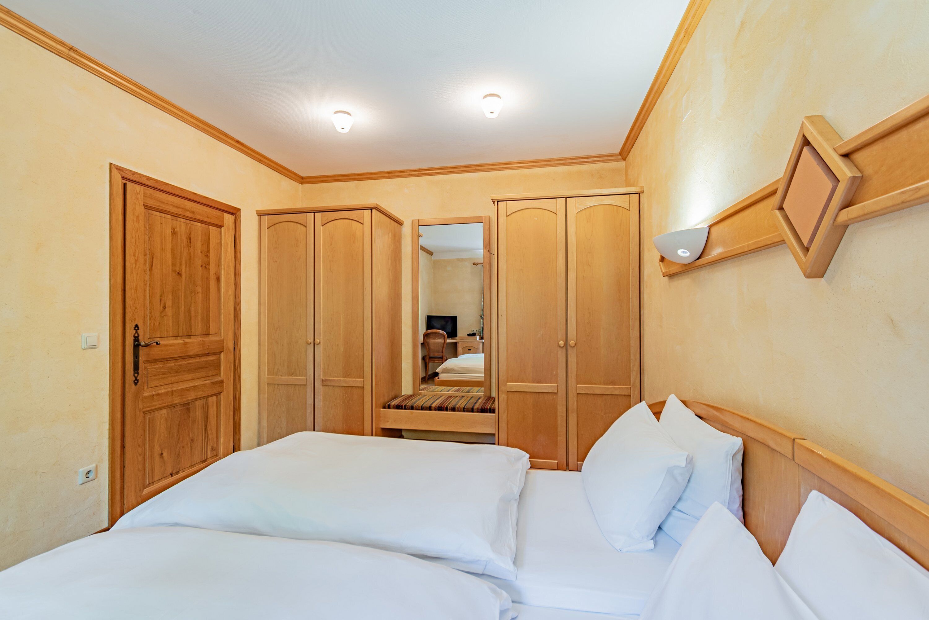 A bedroom with a bed, wooden wardrobe, and a mirror.