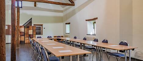 A conference room with long tables and chairs, wooden beams on the ceiling, and a tiled floor.