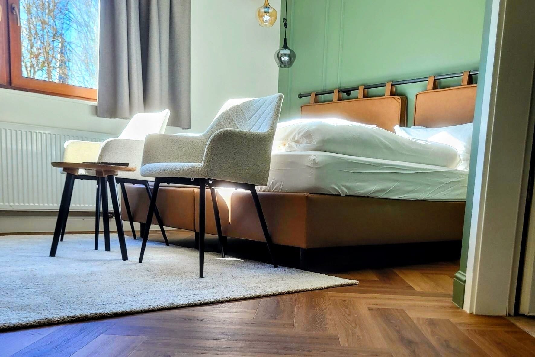 A bedroom with a bed, two chairs, a small table, and a window with curtains.