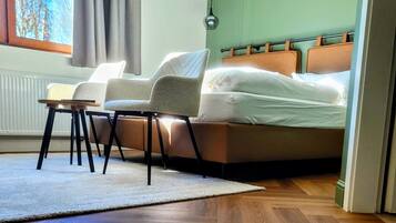 A bedroom with a bed, two chairs, a small table, and a window with curtains.