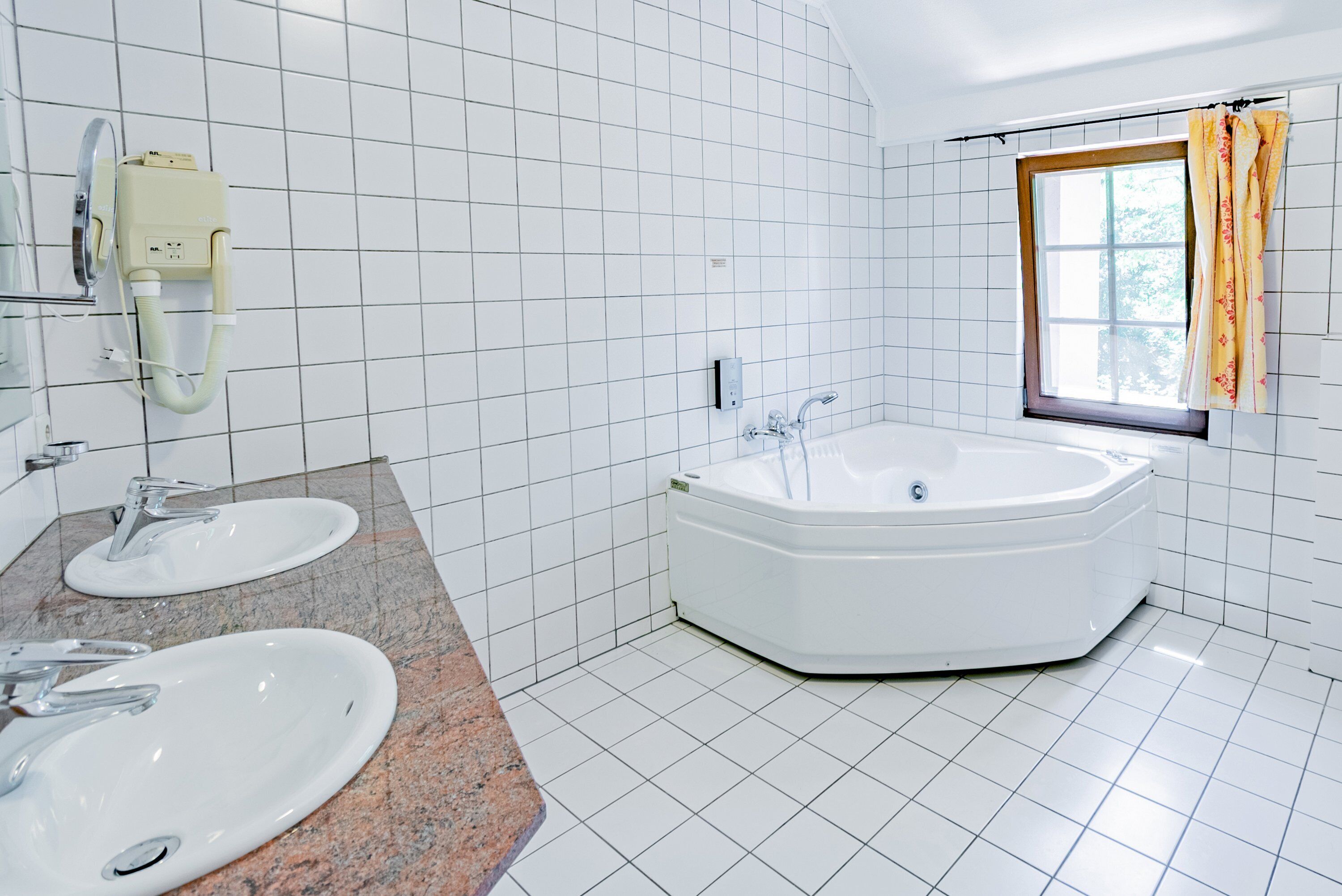 A bathroom with two sinks, a bathtub, and a window with curtains.