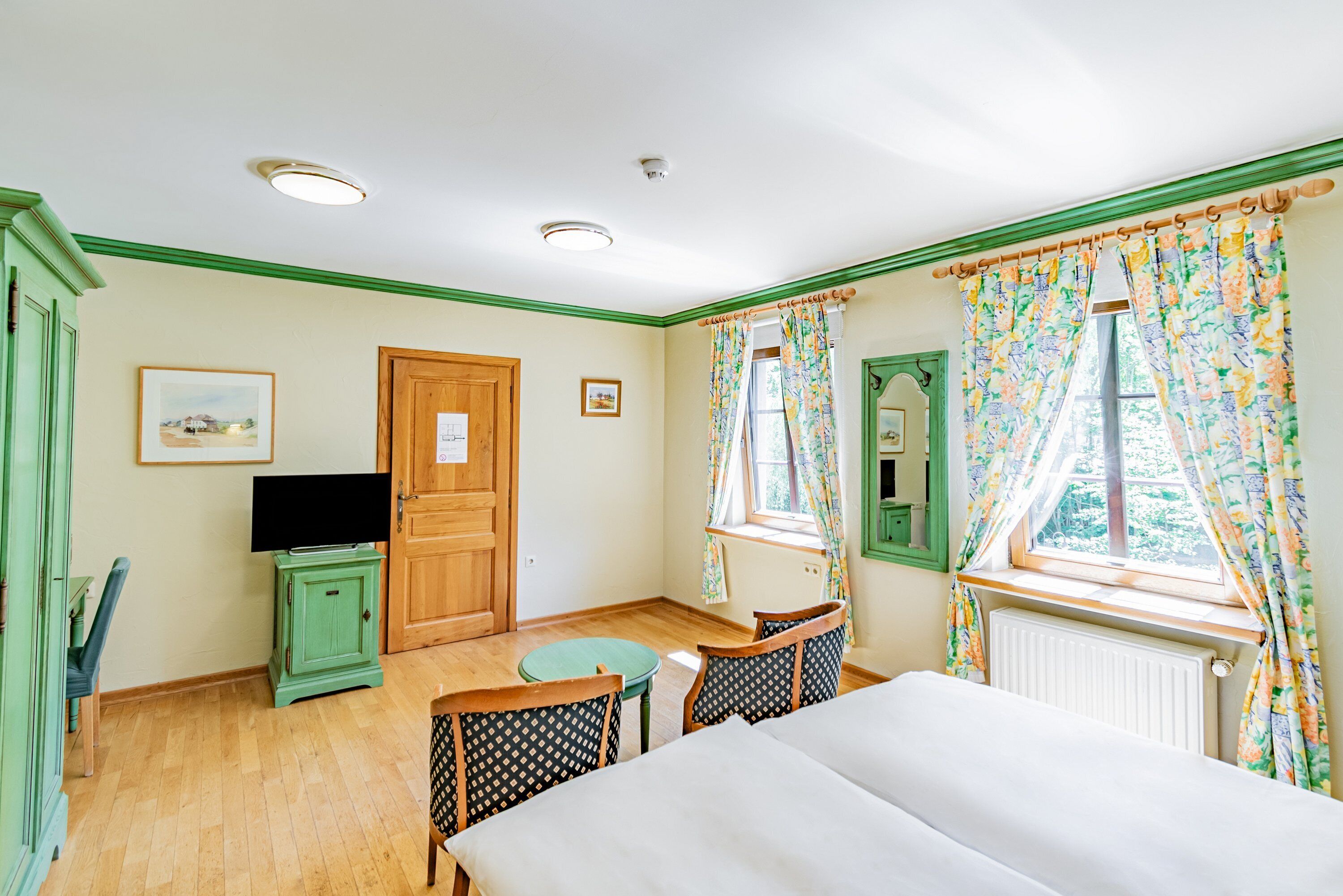 A room with a bed, a small table, two chairs, a television, and a window with curtains.
