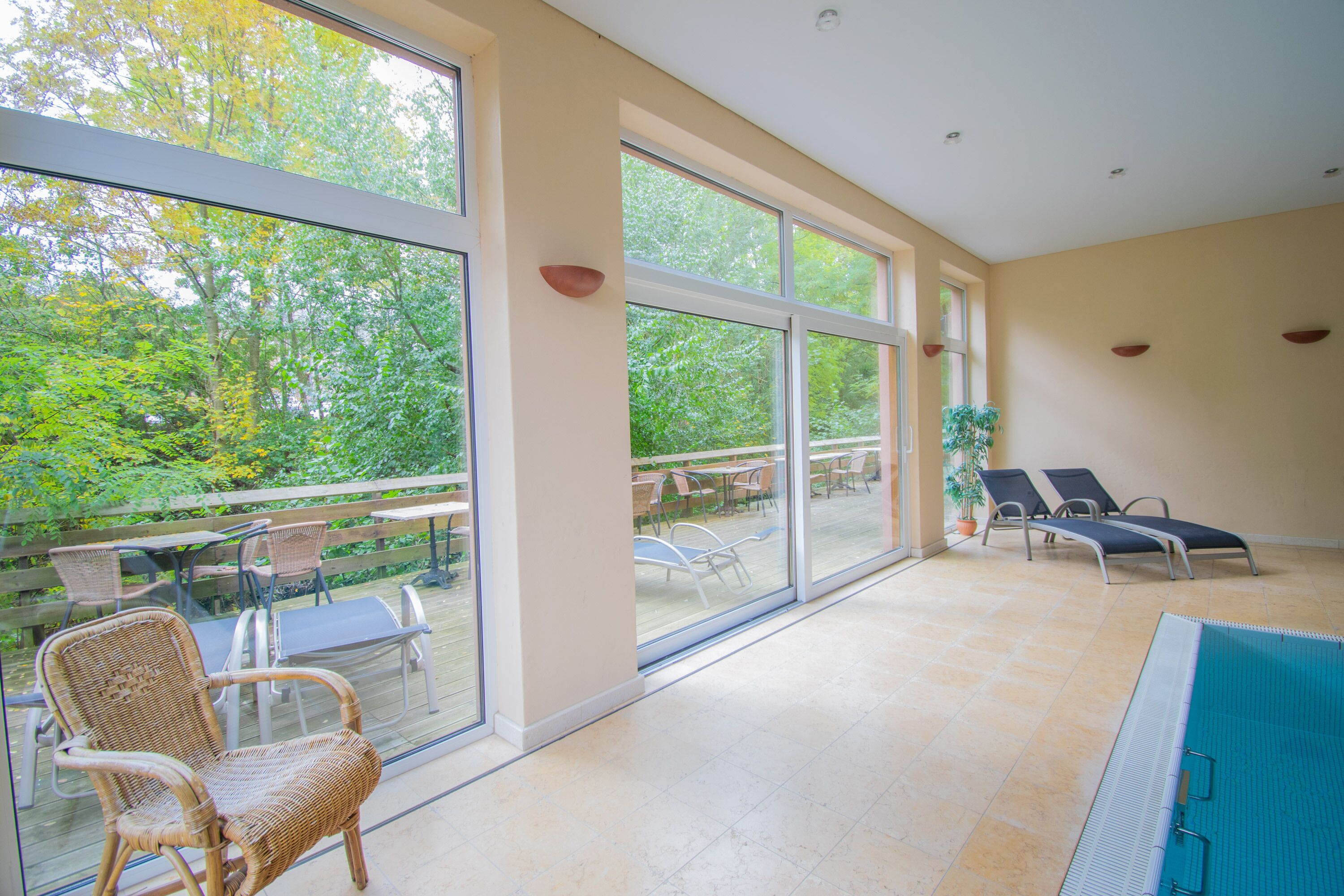 Un espacio interior amplio con grandes ventanales, una piscina y mobiliario de exterior.