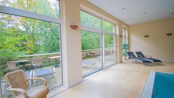 Un espacio interior amplio con grandes ventanales, una piscina y mobiliario de exterior.