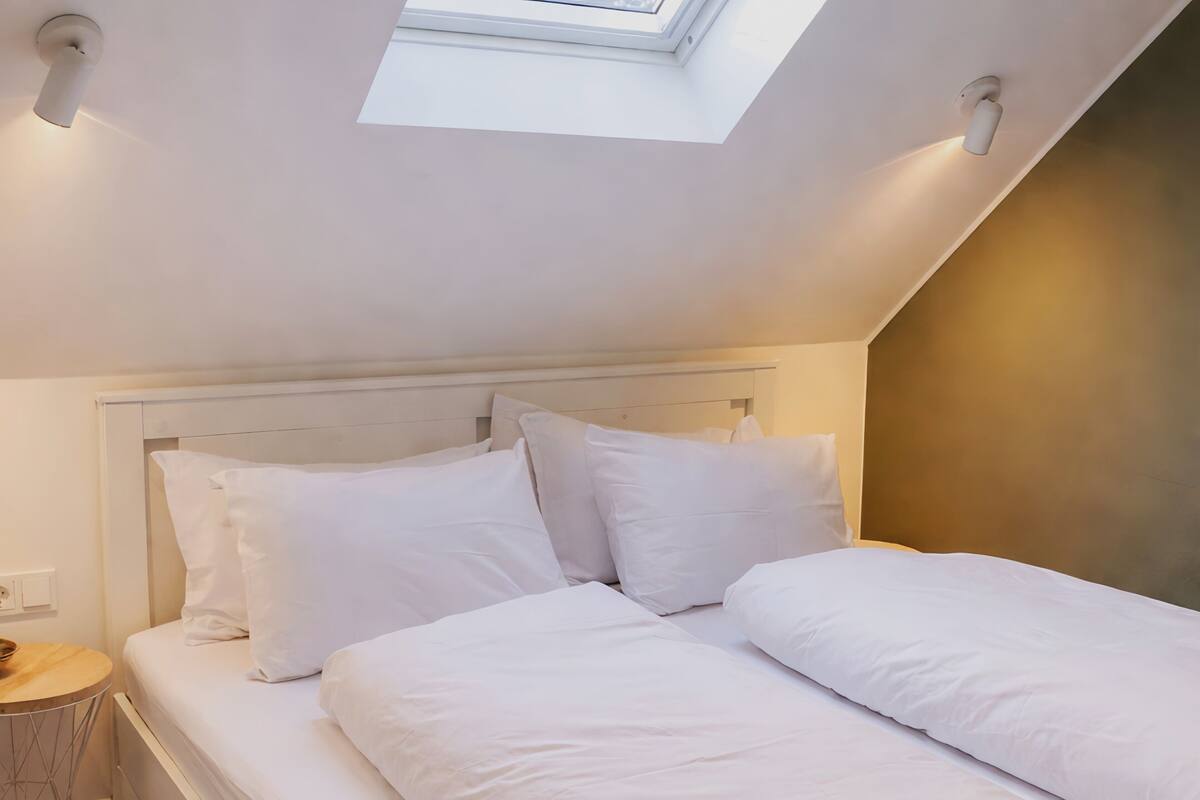 Ein Schlafzimmer mit Dachfenster, einem Bett mit weißer Bettwäsche und einem Nachttisch.