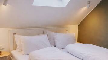A bedroom with a skylight, a bed with white bedding, and a bedside table.