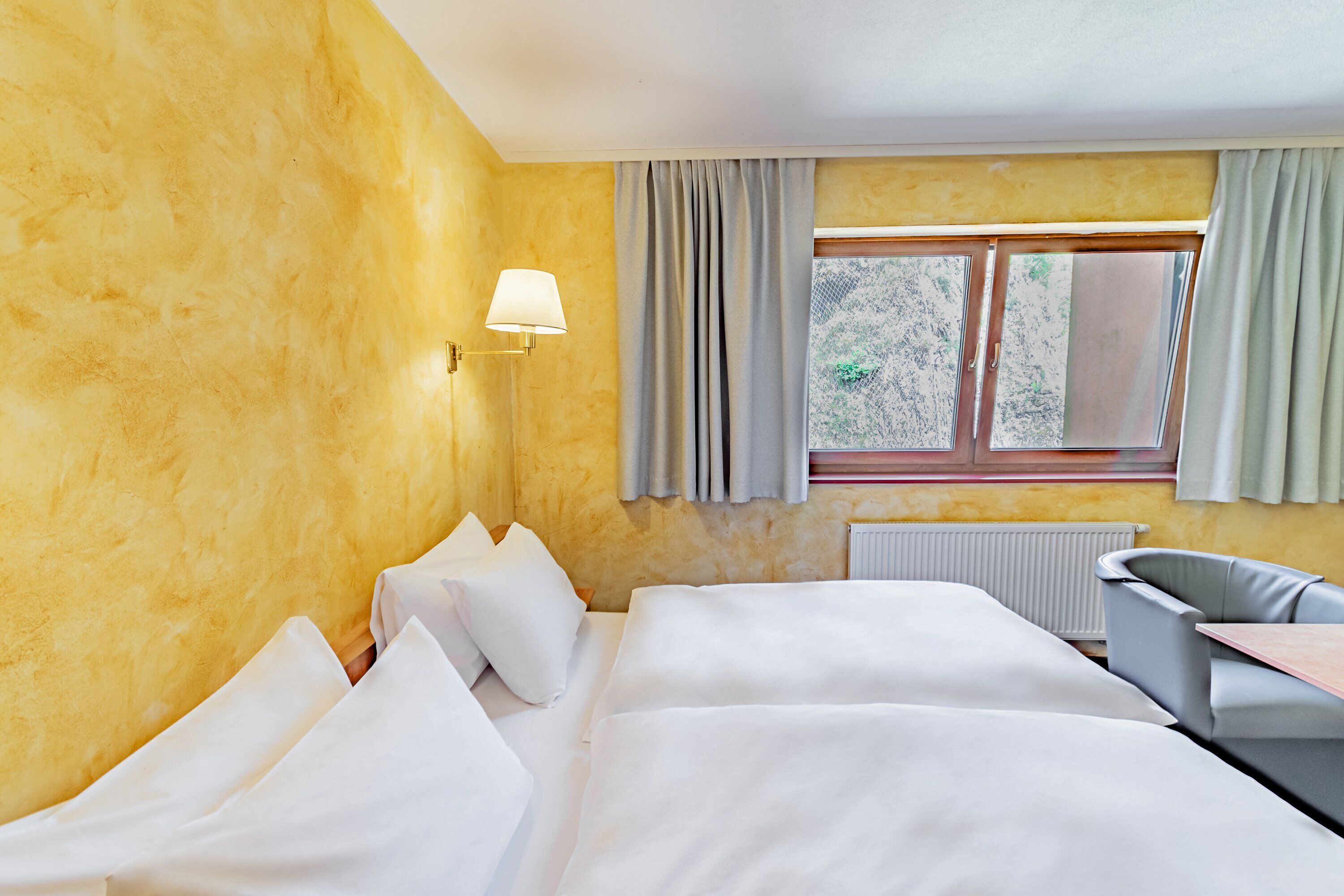 A hotel room with a bed, a desk, a chair, and a window with curtains.