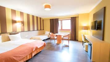 A hotel room with two beds, a dining table with chairs, a TV, and a window with curtains.
