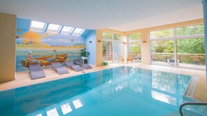 Une piscine intérieure ornée d’une fresque représentant un soleil et un bateau, avec des chaises longues et de grandes fenêtres offrant une vue sur l’extérieur.