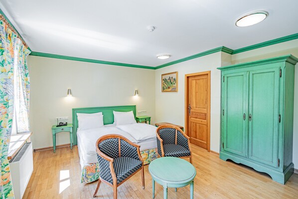 Una habitación con una cama, dos sillas, una mesa, un armario y un cuadro en la pared.