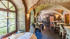 Un intérieur agrémenté d’arches en pierre, de tables et de chaises en bois, et d’une grande fenêtre offrant une vue sur les arbres.
