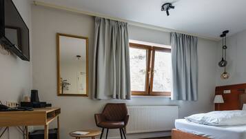 A bedroom with a bed, a desk, a chair, a window with curtains, a radiator, and a ceiling light fixture.