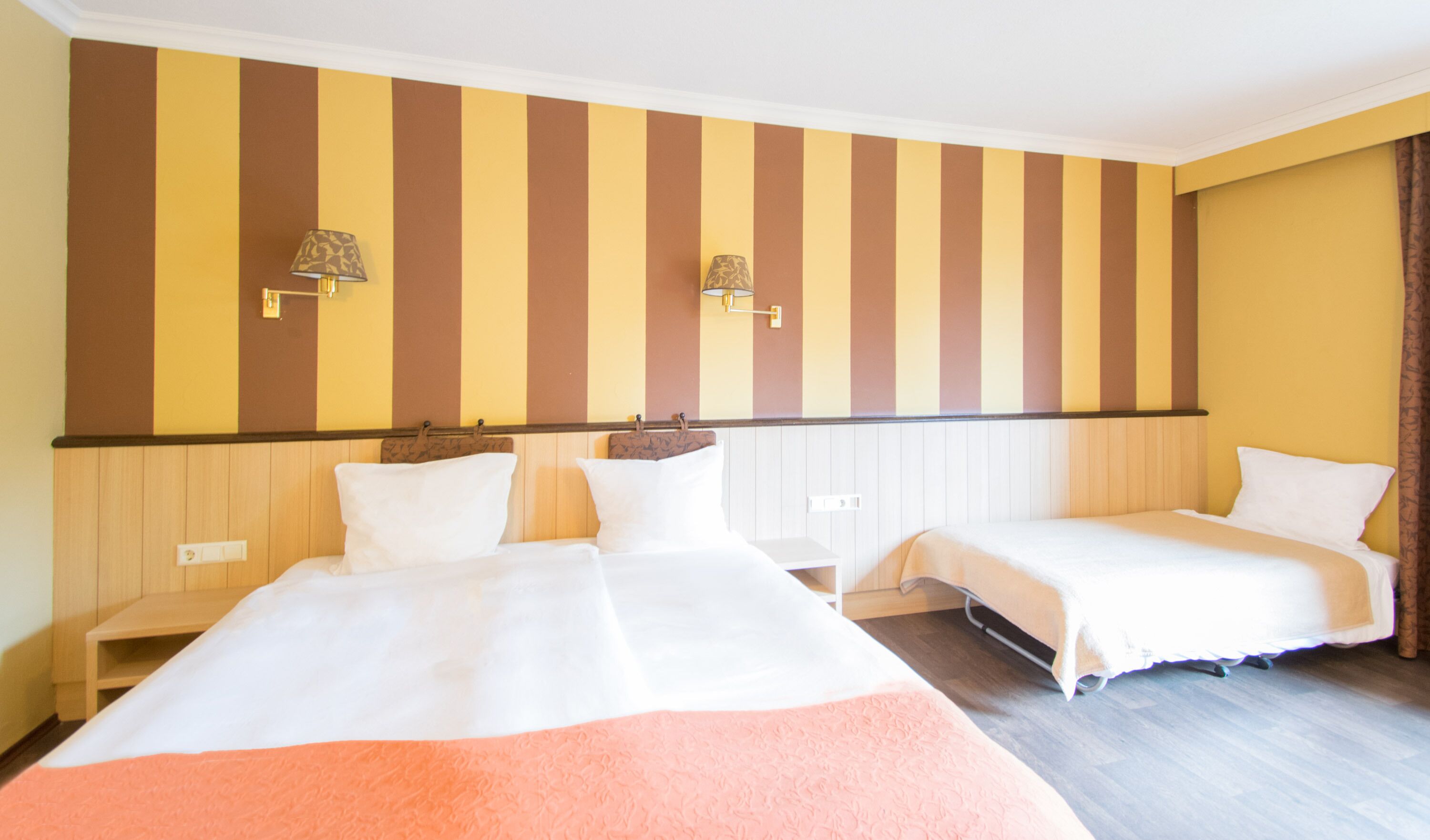 Habitació d'hotel amb dos llits, paper pintat a ratlles i làmpades penjades a la paret.