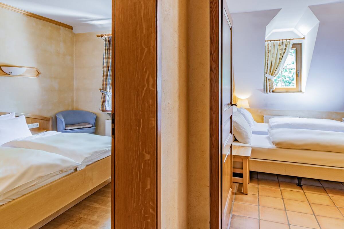 Ein Hotelzimmer mit zwei Betten, einem Holzkopfstück, einem kleinen Stuhl, einem Nachttisch und einem Fenster mit Vorhängen.