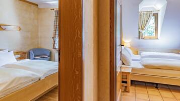 Ett hotellrum med två sängar, en sänggavel i trä, en liten stol, ett nattduksbord och ett fönster med gardiner.