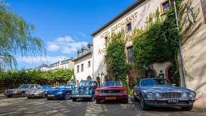 Une rangée de voitures anciennes est garée devant un bâtiment sur lequel on peut lire l’inscription « Hôtel Restaurant Ancien ».