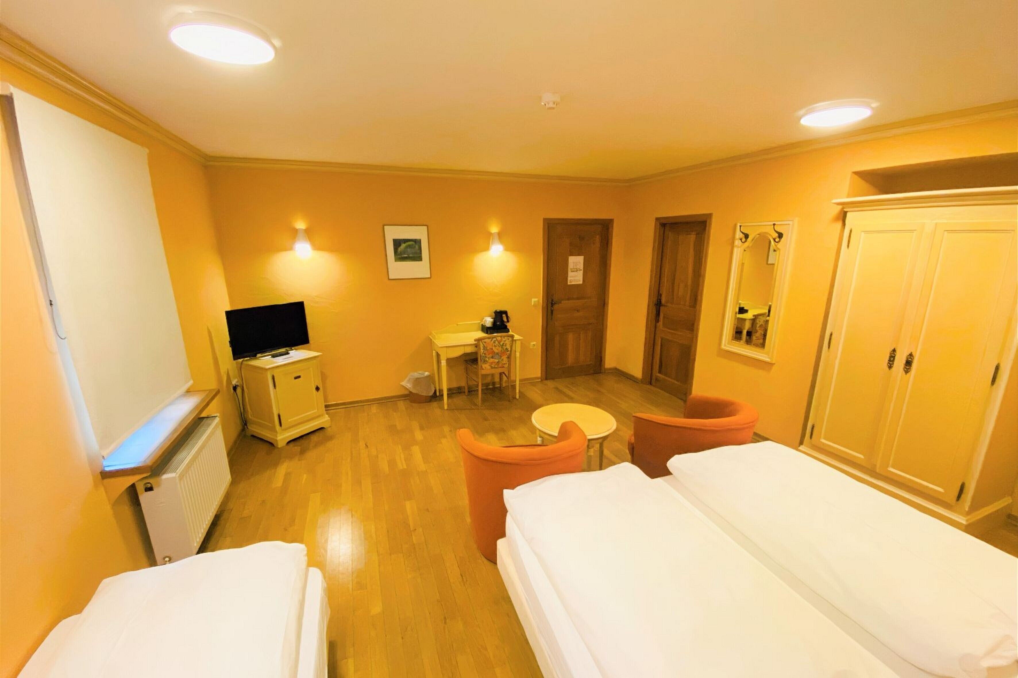 A hotel room with two beds, a desk, a chair, a radiator, a television, and a wardrobe.