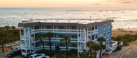 A multi-story hotel with a rooftop pool, located near a beach with a view of the ocean.