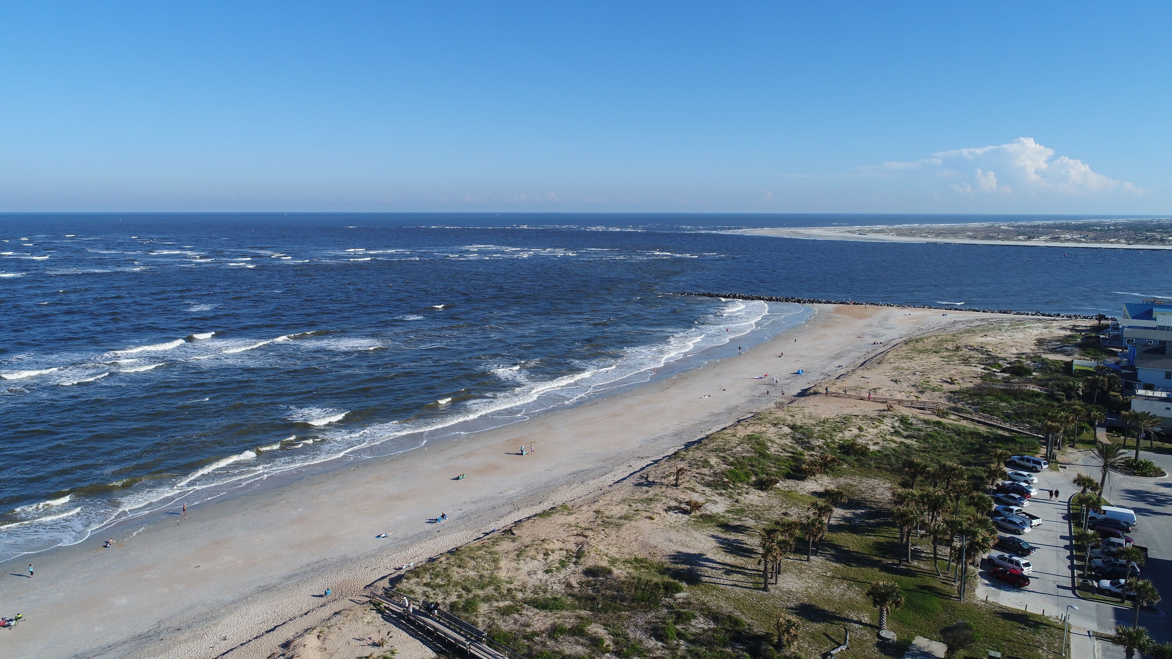 A beach with a wooden walkway, a parking area, and a view of the ocean.