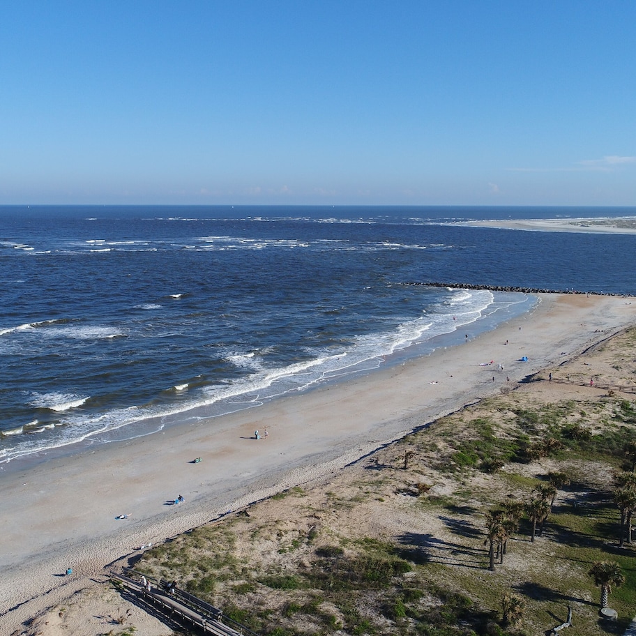 A beach with a wooden walkway, a parking area, and a view of the ocean.