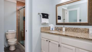 A bathroom with a toilet, shower, vanity with a mirror, and towels.