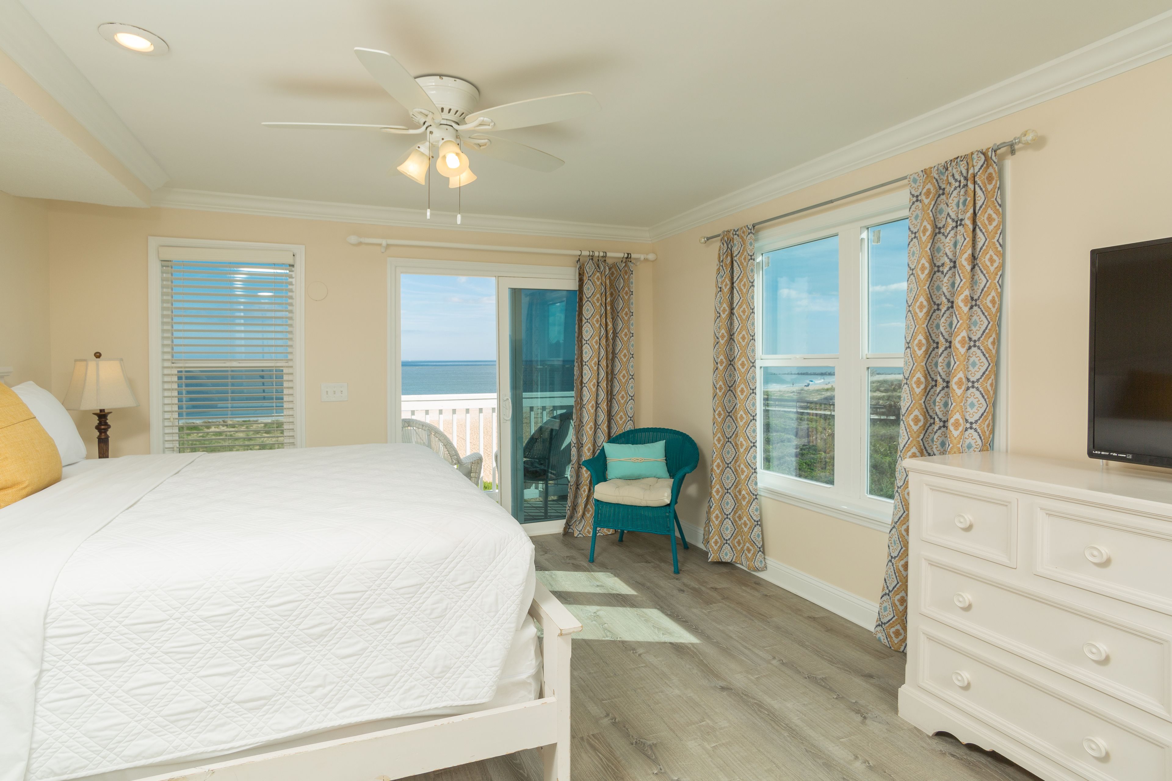 A bedroom with a bed, a dresser, a television, a chair, and a balcony with a view.