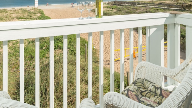 A balcony with wicker furniture overlooking a beach.