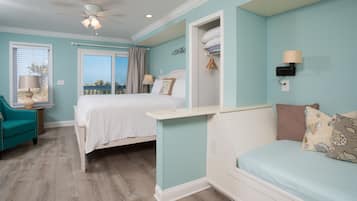 A bedroom with a bed, a chair, a bedside table, a ceiling fan, and a view through a window.