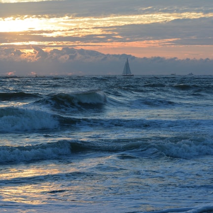 A sailboat on a choppy sea with a sunset in the background.