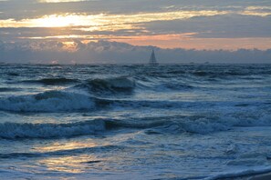 A sailboat on a choppy sea with a sunset in the background.