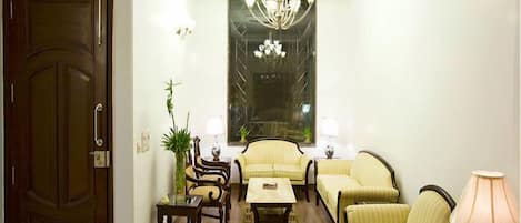 Un salon bien éclairé, agrémenté d’un lustre, de fauteuils à rayures, d’un canapé et d’une table sur laquelle sont posées des théières.