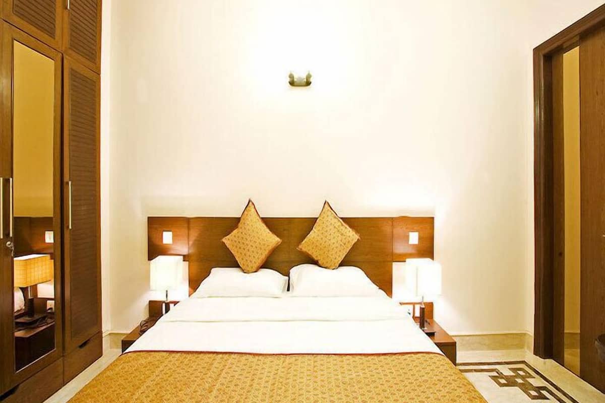 A hotel room with a large bed, two bedside tables with lamps, a wooden headboard with decorative elements, and a patterned area rug.