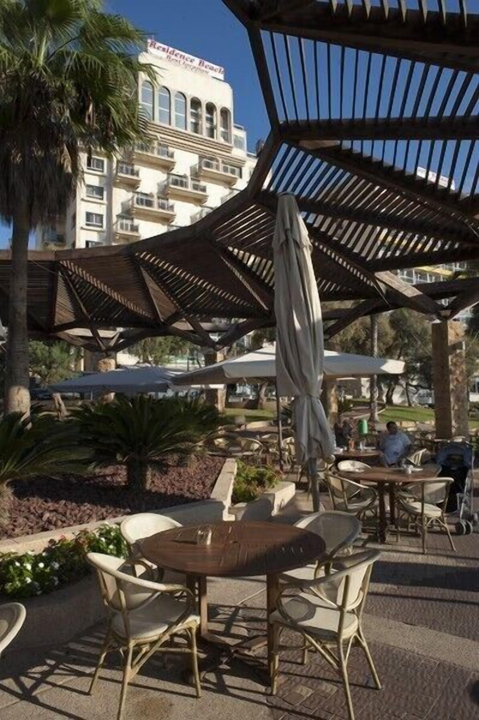 An outdoor patio area with wicker furniture, umbrellas, and a view of a building labeled "Residence Beach."