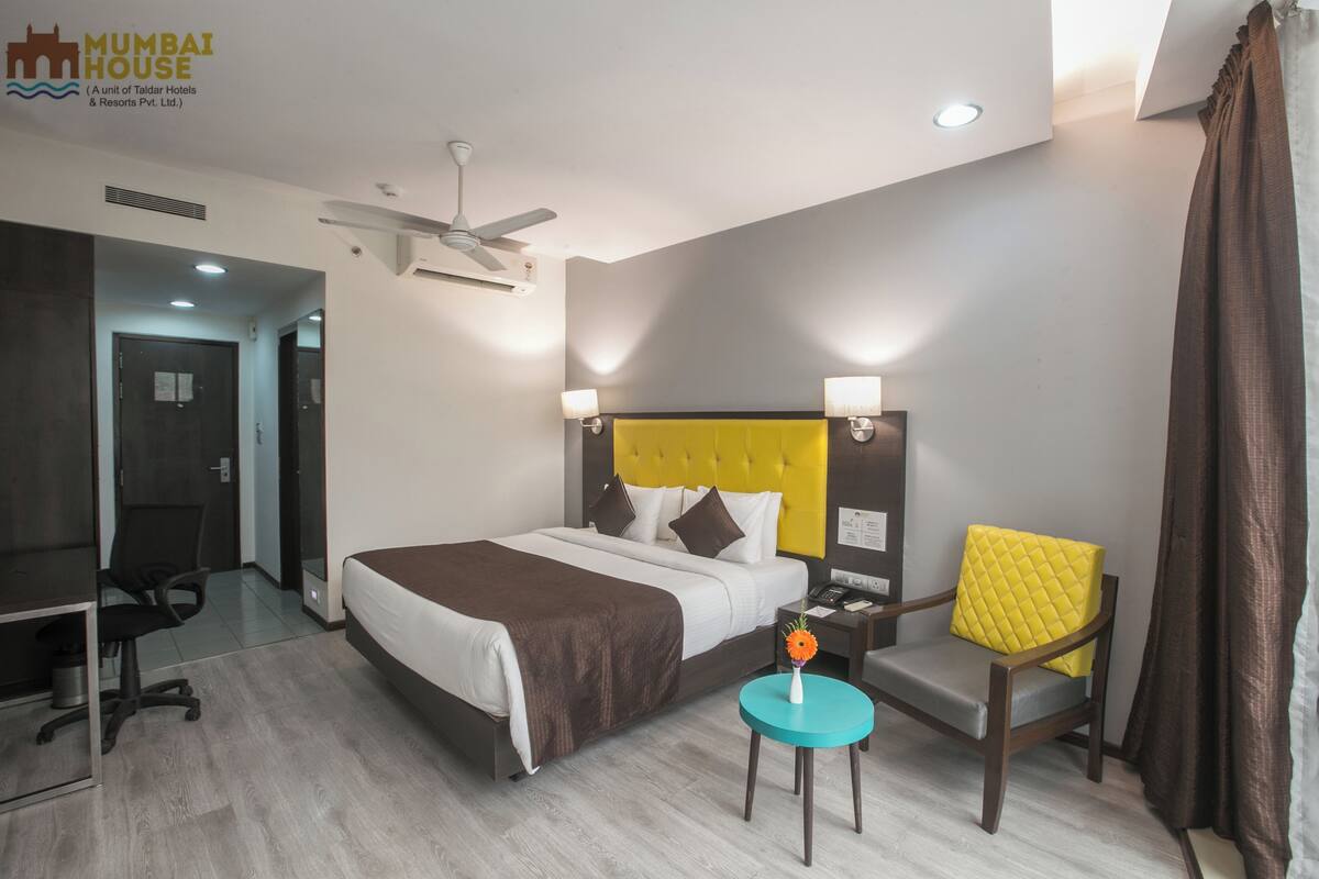 Ein Hotelzimmer mit Bett, Schreibtisch, Stuhl, kleinem Tisch und Deckenventilator.