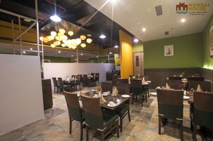 Un restaurante con varias mesas y sillas, un techo con luces colgantes y una pared verde con un logotipo.