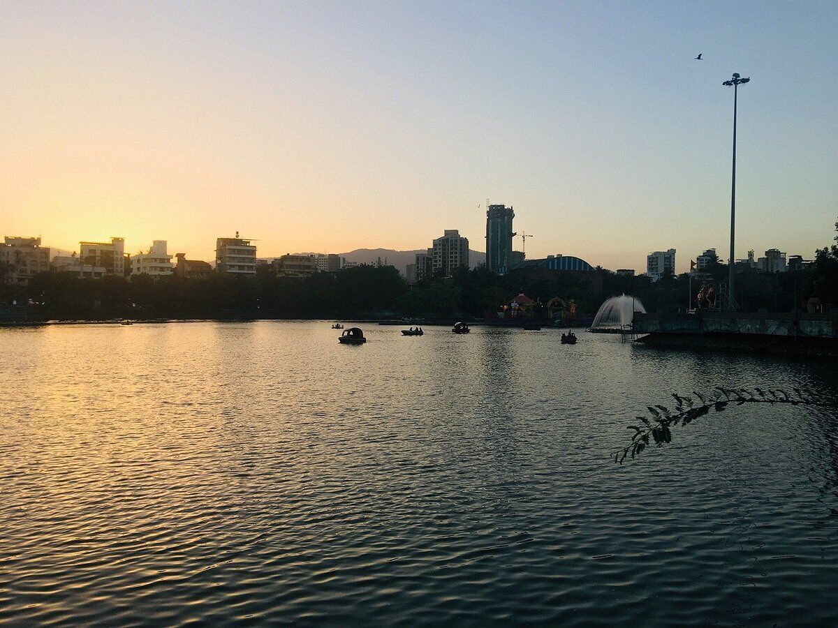 A sunset view of a cityscape with buildings, a fountain, and boats on the water.