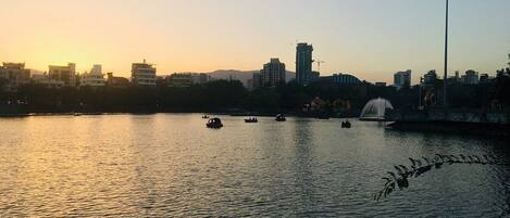 A sunset view of a cityscape with buildings, a fountain, and boats on the water.