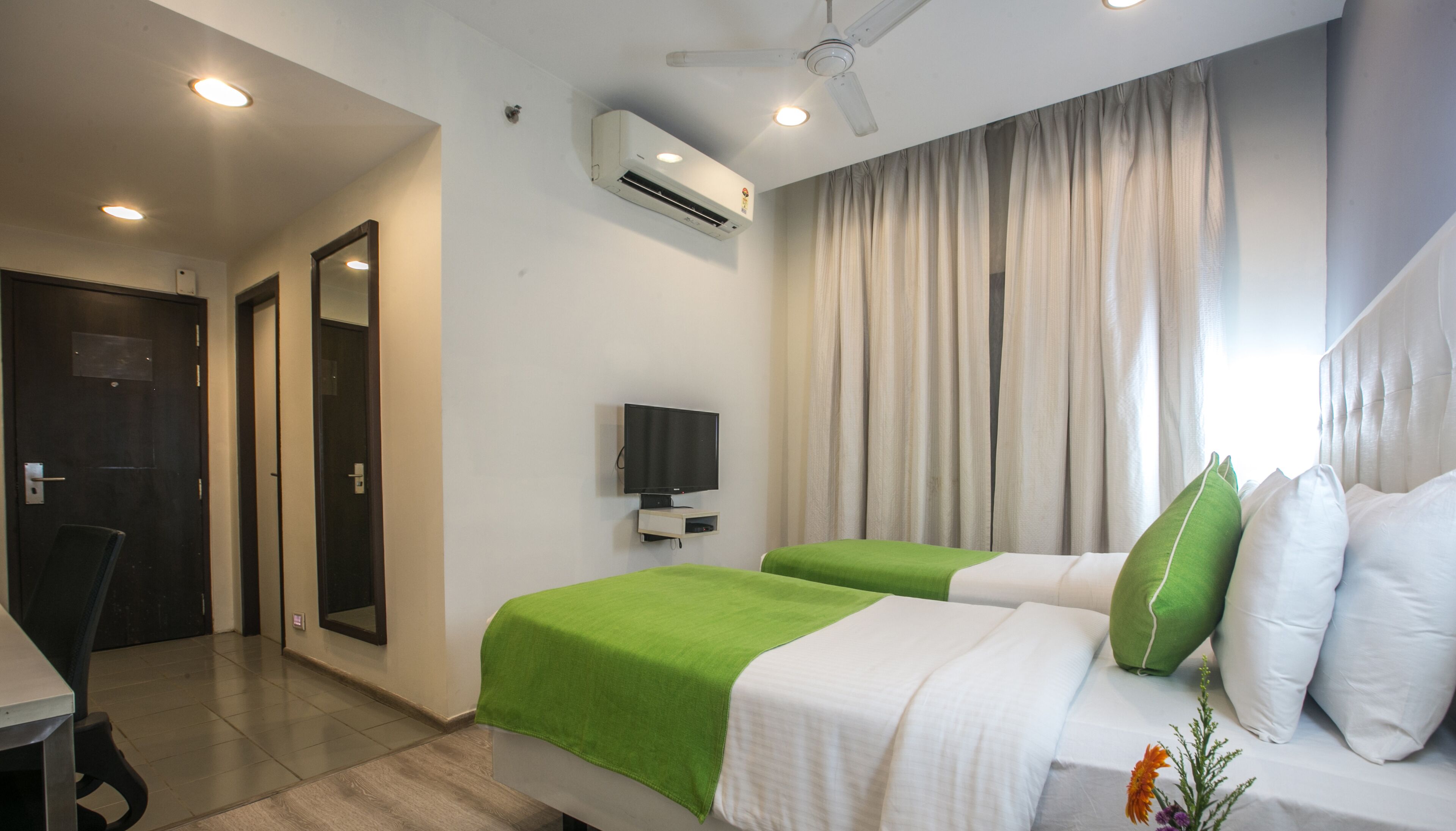 Une chambre d’hôtel avec deux lits, une télévision, un climatiseur et un ventilateur de plafond.