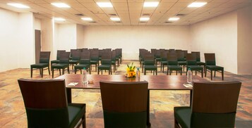 Un salón de conferencias con una larga mesa y sillas, equipado con botellas de agua y un centro de mesa floral.