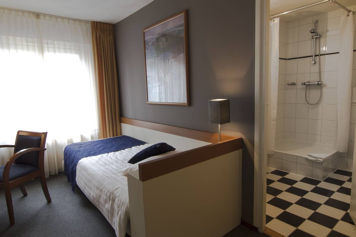 Una habitación de hotel con cama, una silla, ducha y un cuadro en la pared.