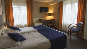 Habitación de hotel con dos camas, un escritorio, una silla, un televisor y cortinas.