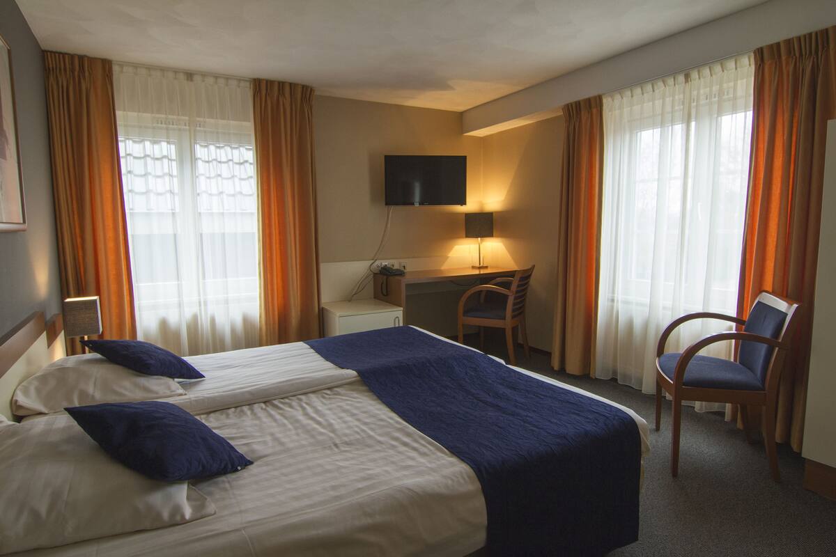 Habitación de hotel con dos camas, un escritorio, una silla, un televisor y cortinas.