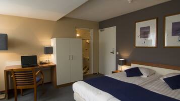Een hotelkamer met een bed, bureau, stoel en een deur naar een badkamer.