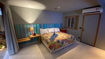 Un dormitorio con una cama, una mesita de noche con lámpara, una pared de rayas coloridas y una puerta con unidad de aire acondicionado.